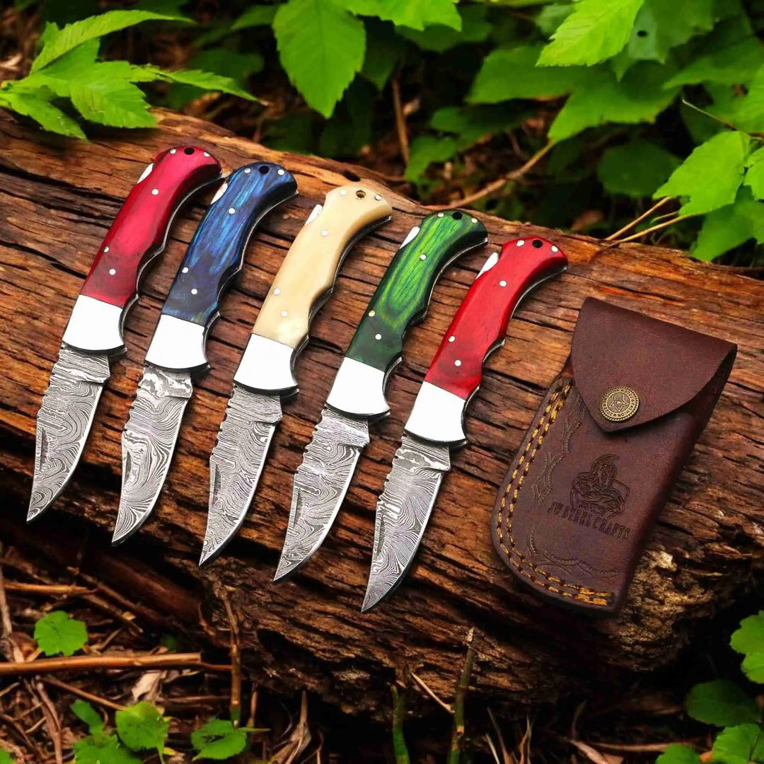     Pinevalley Damascus folding knives with hardwood finishes and detailed steel patterns beside leather pouch