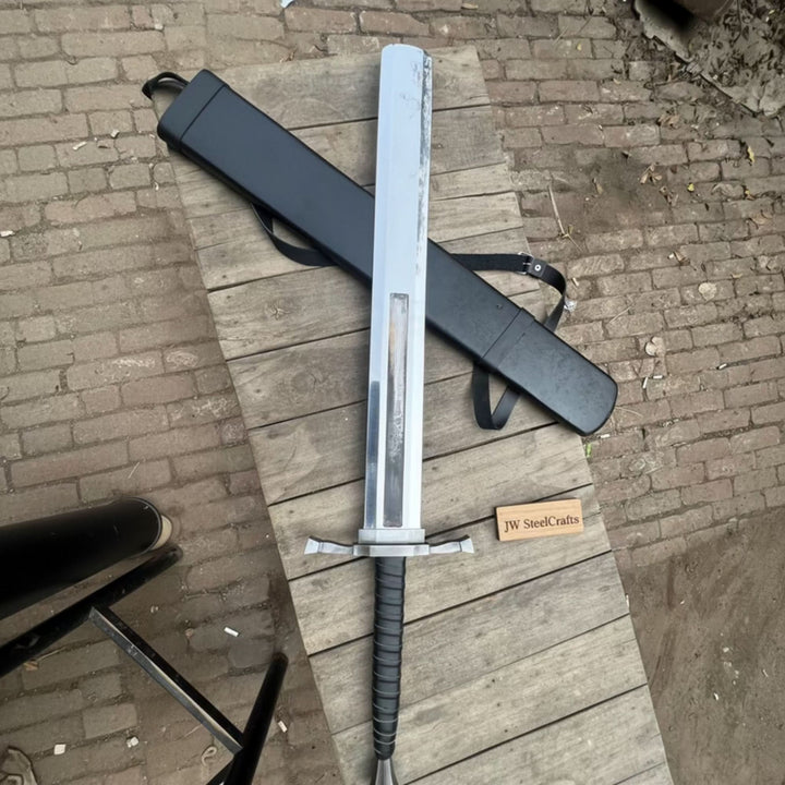 Cosplay Dragon Slayer greatsword replica with a wide slab blade, black cord-wrapped grip, and black carry case on a wood plank