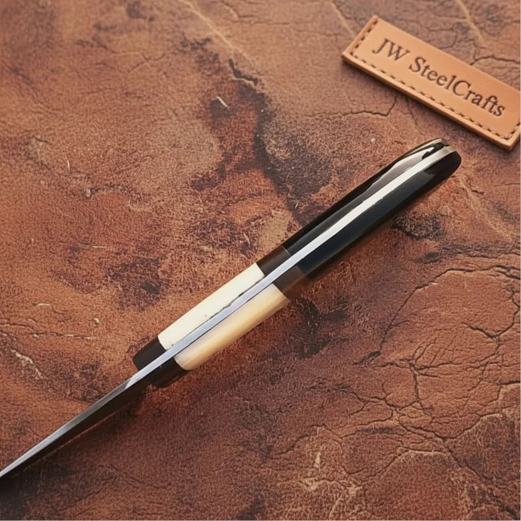Closeup side profile of handcrafted chef knife handle featuring polished black and ivory grip with visible full tang construction.