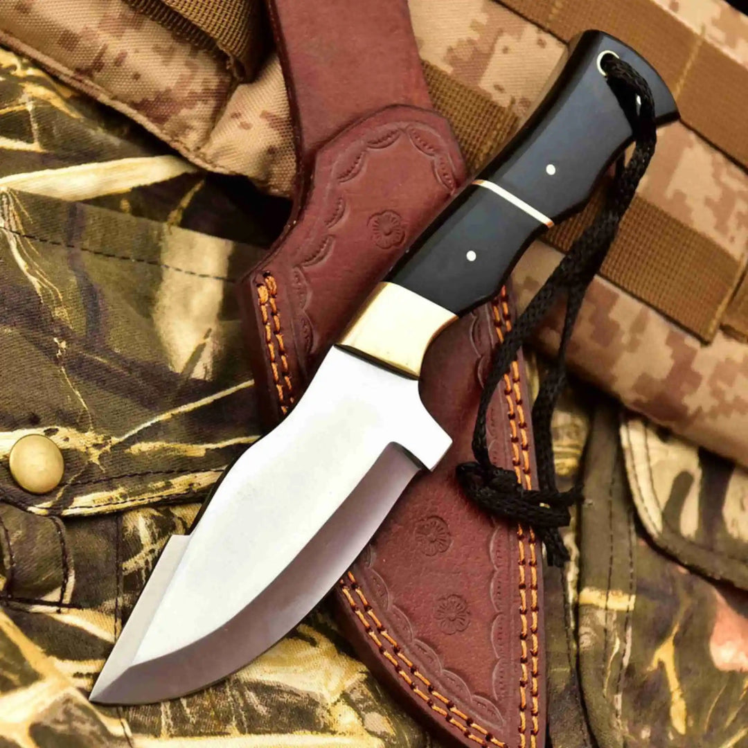 Handmade fixed blade knife featuring a black handle, white pins, brass accents, black lanyard, and brown leather sheath.
