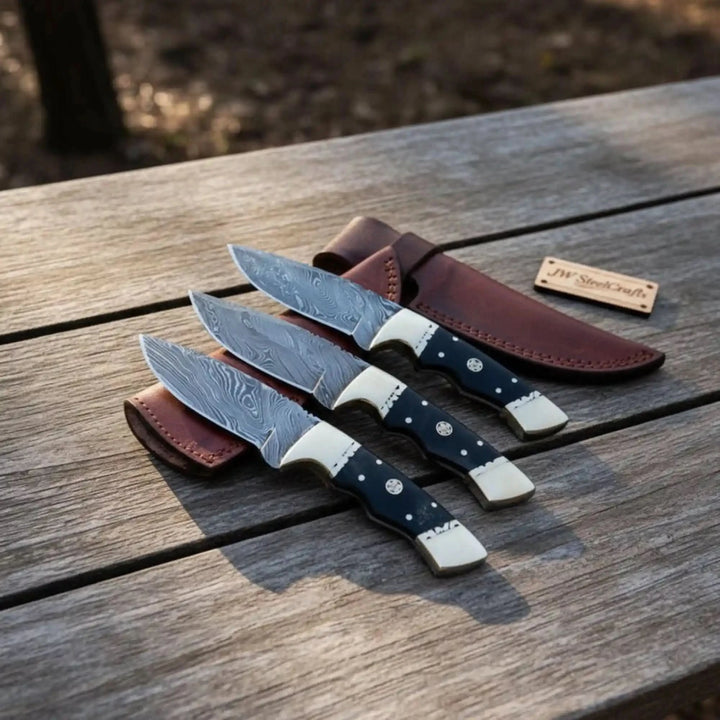 Tactical throwing knives with black grips, slim steel blades, silver handle fittings, and brown leather sheath.