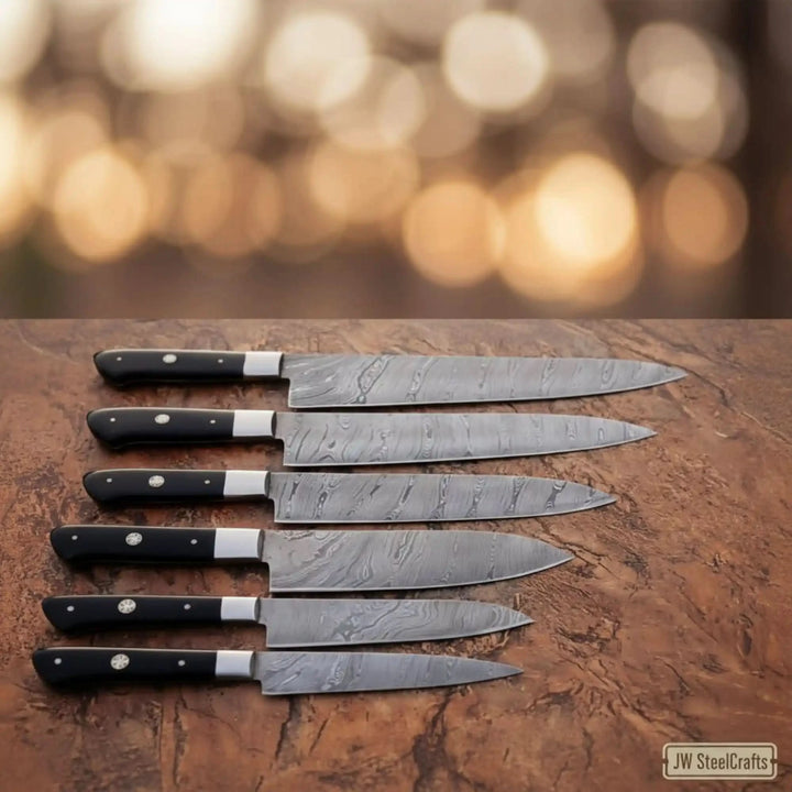Elegant product shot of JW SteelCrafts Damascus carving slicer knife collection with black resin handles and polished steel bolsters arranged on rustic leather surface against warm golden bokeh
