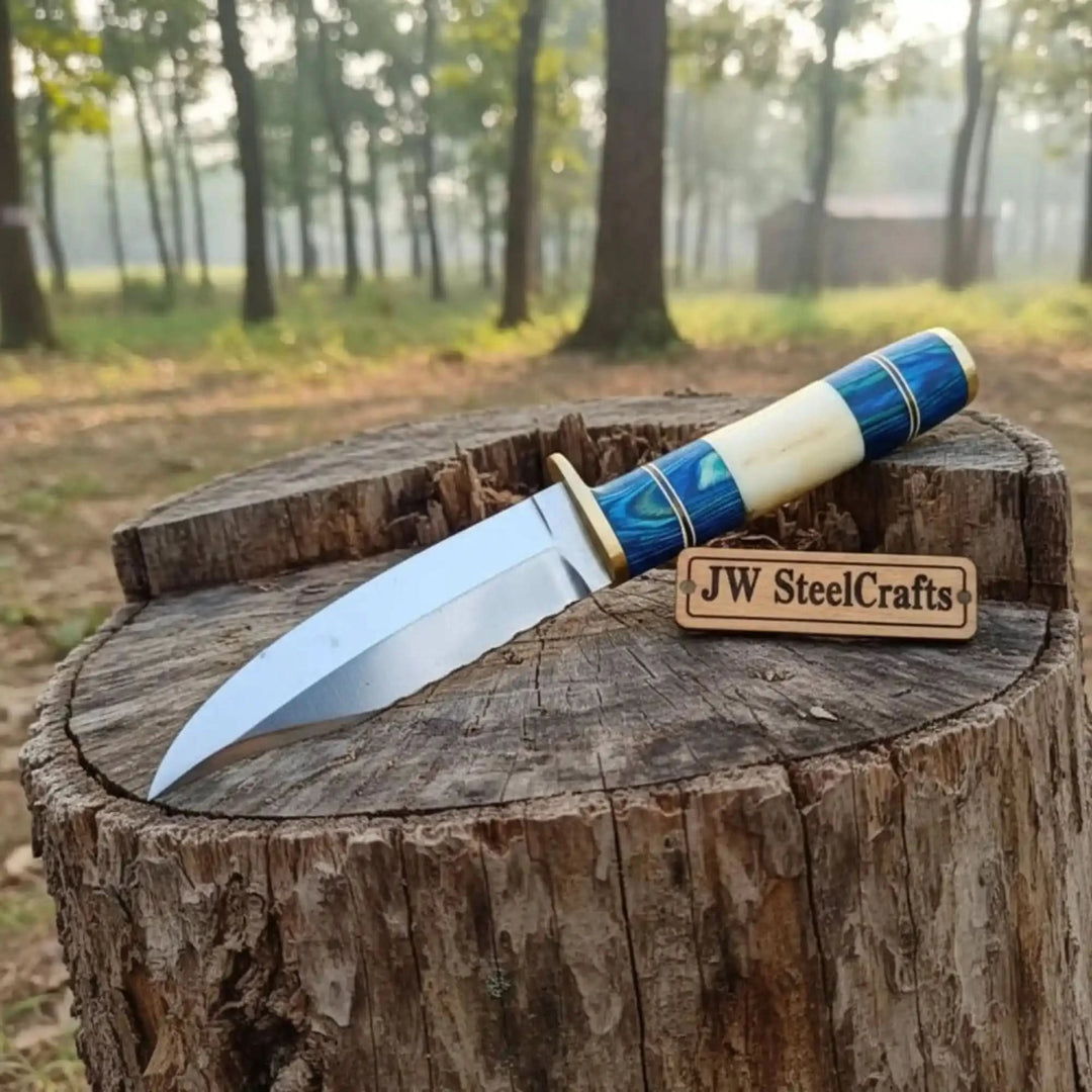 Handmade outdoor Bowie knife featuring a blue and cream handle, sharp polished blade, and forest stump display.