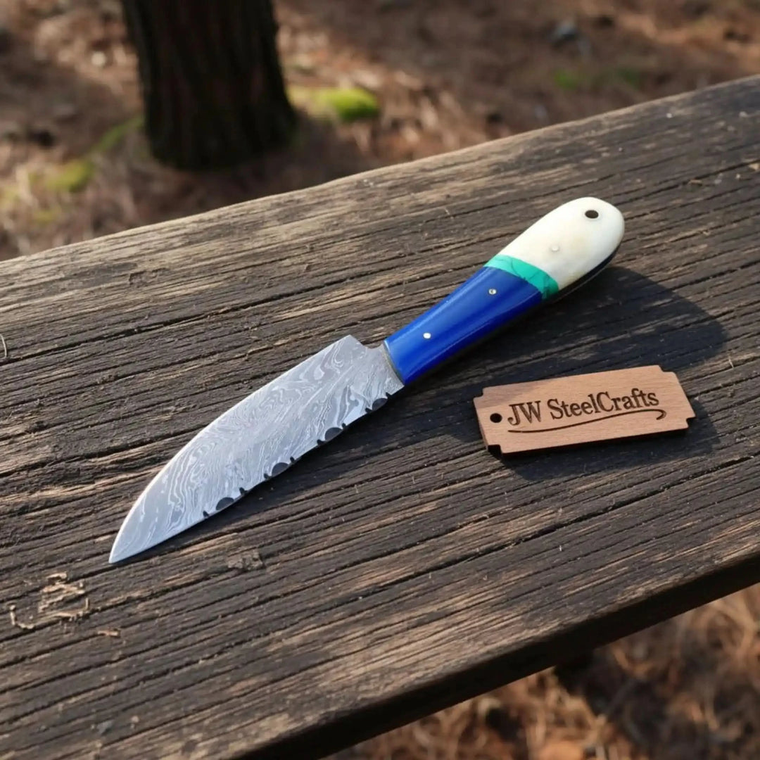 Damascus drop point knife with blue handle scales, white end cap, turquoise spacer, and forest wood table display.