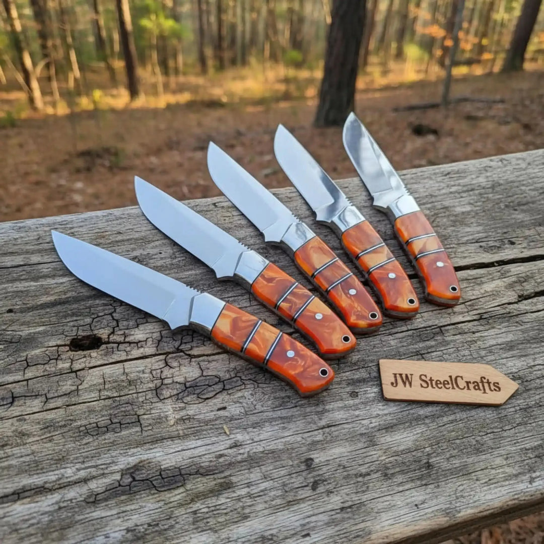 Precision-crafted with serrated spine guards and orange swirl handles, five artisan knives fan on a rustic forest stump