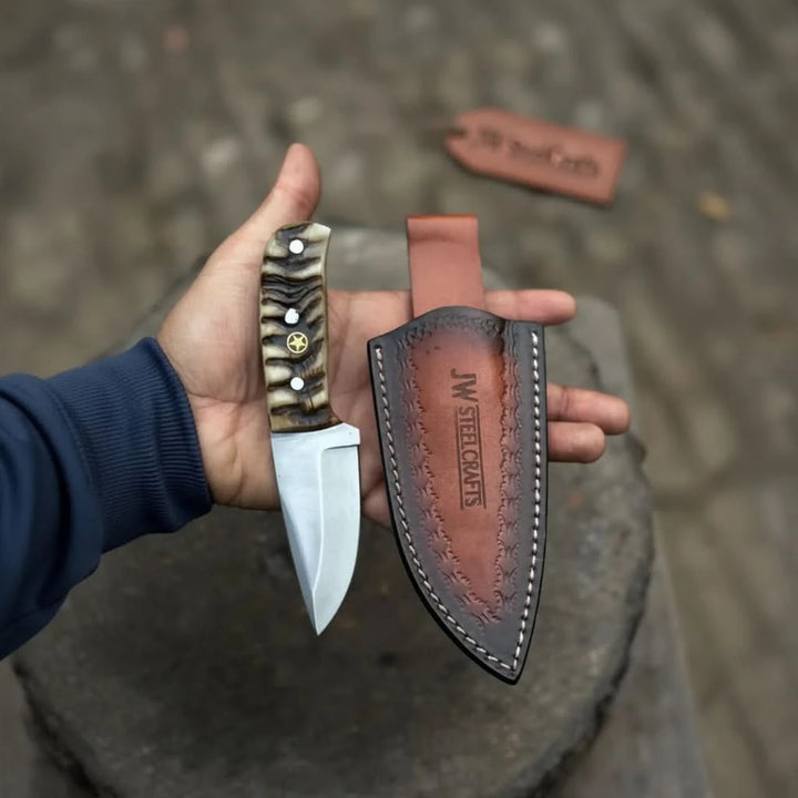 Small skinner knife with bone style handle, polished drop point blade, and brown stitched leather sheath.