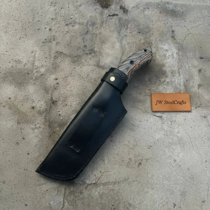 Custom Damascus cleaver knife product photo showing black sheath, patterned blade, hand grip, and carved handle scales.
