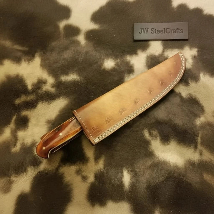 Leather sheath Damascus kitchen blade displayed on a walnut butcher block in a kitchen