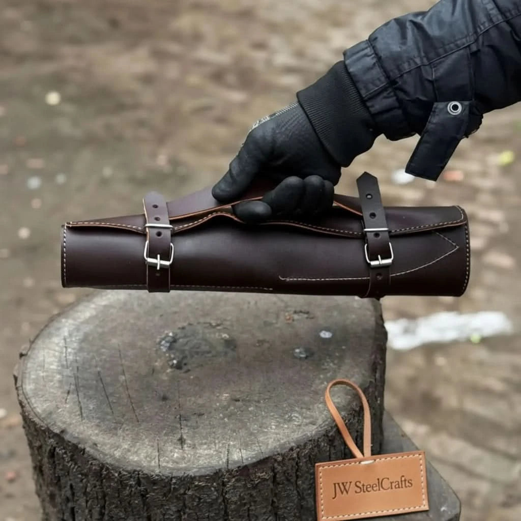 Closed full-grain dark brown leather chef knife roll case with two silver buckle closures and white stitching, held by a gloved hand in an outdoor setting
