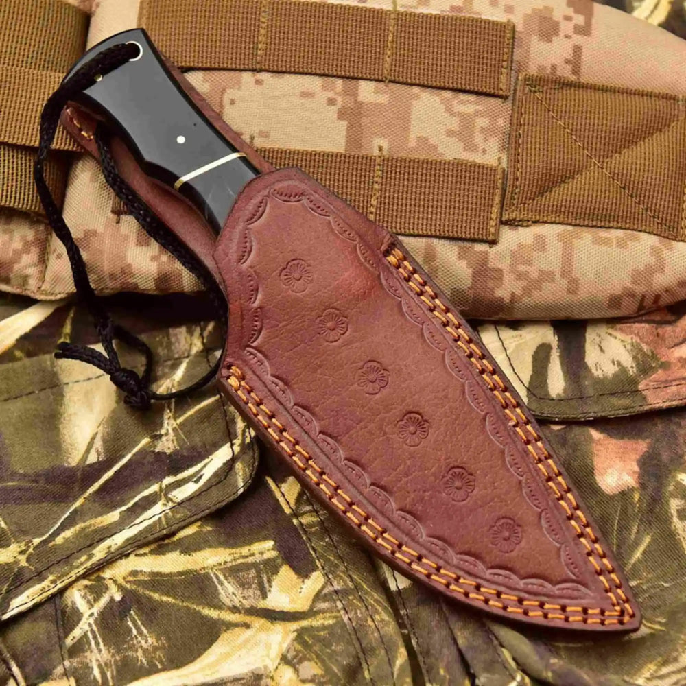 Leather sheath fixed blade knife with lanyard, black handle, brass bolster, and polished drop point blade.
