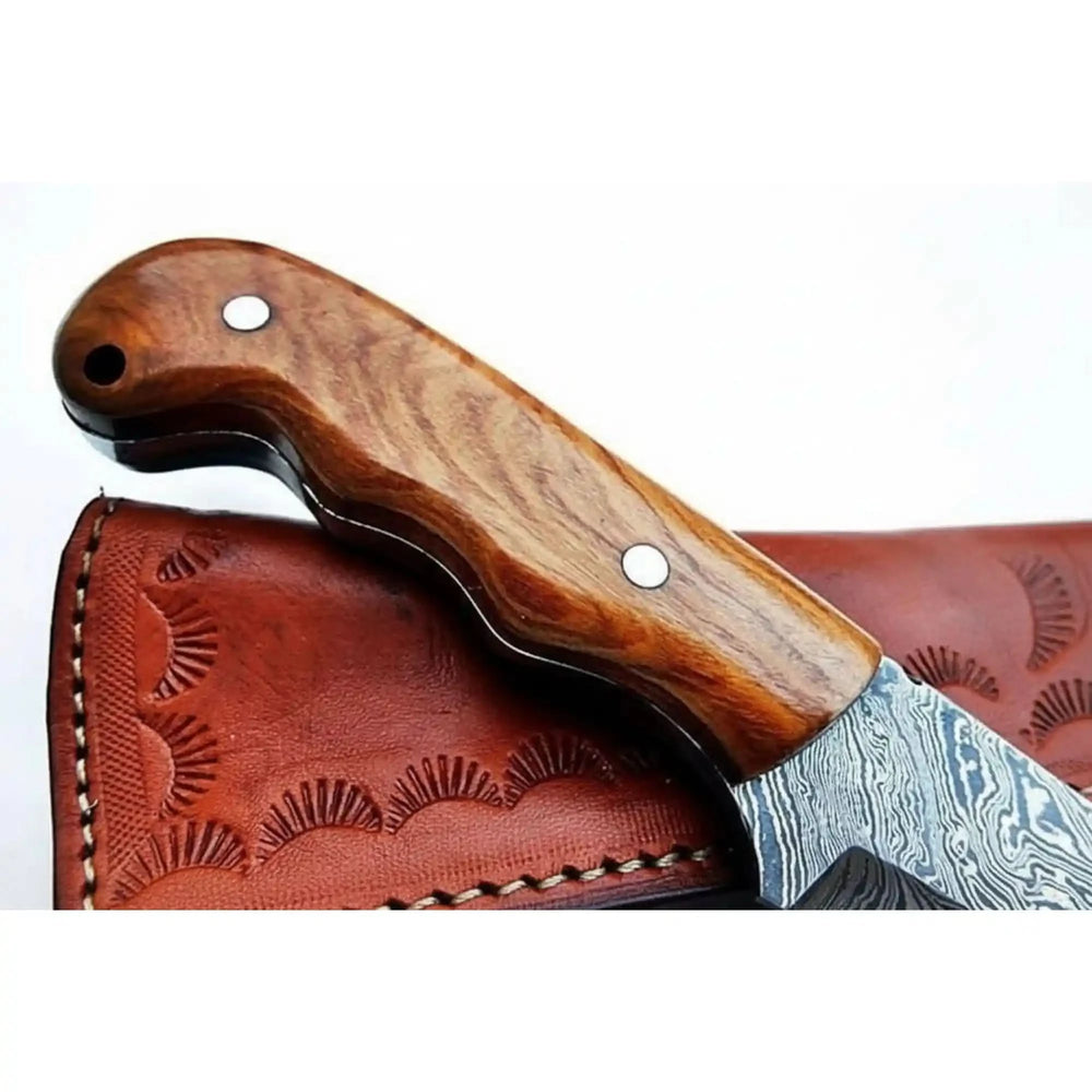 Compact Damascus field knife with wood grip, drop point blade, leather sheath, and blurred woodland background.