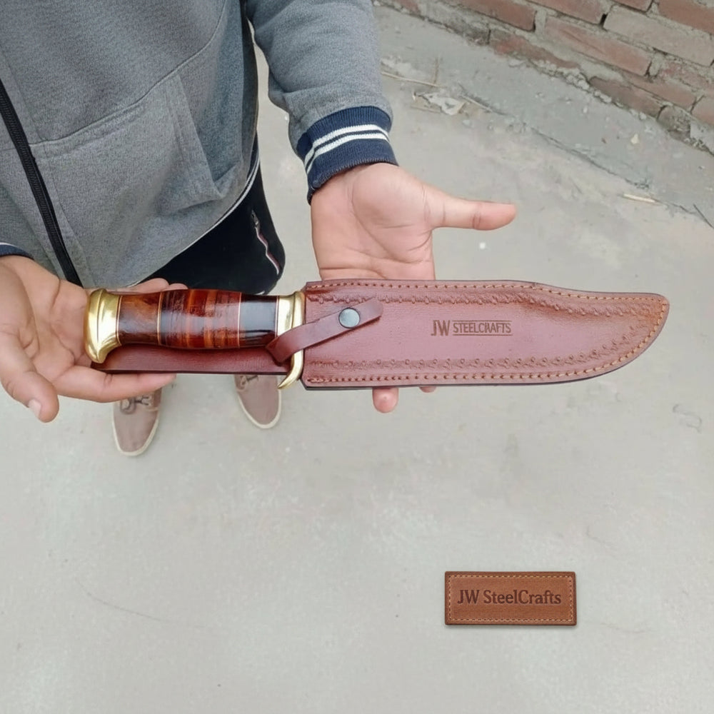 Leather sheath long Damascus Bowie knife with brass guard, stacked wood handle, and rustic forest table display.