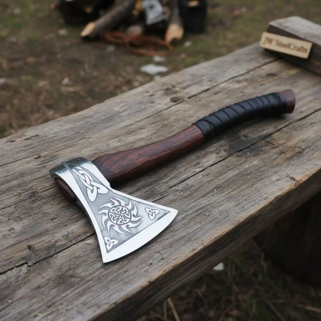 Custom Viking axe with Celtic engraved steel blade and dark wooden handle placed on a rustic outdoor wooden bench 
