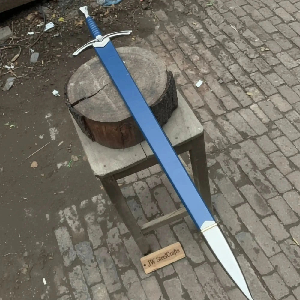 Full-length view of a medieval longsword and matching blue scabbard on a rustic wooden stool on cobblestones, highlighting the silver winged crossguard and blue wrapped handle.