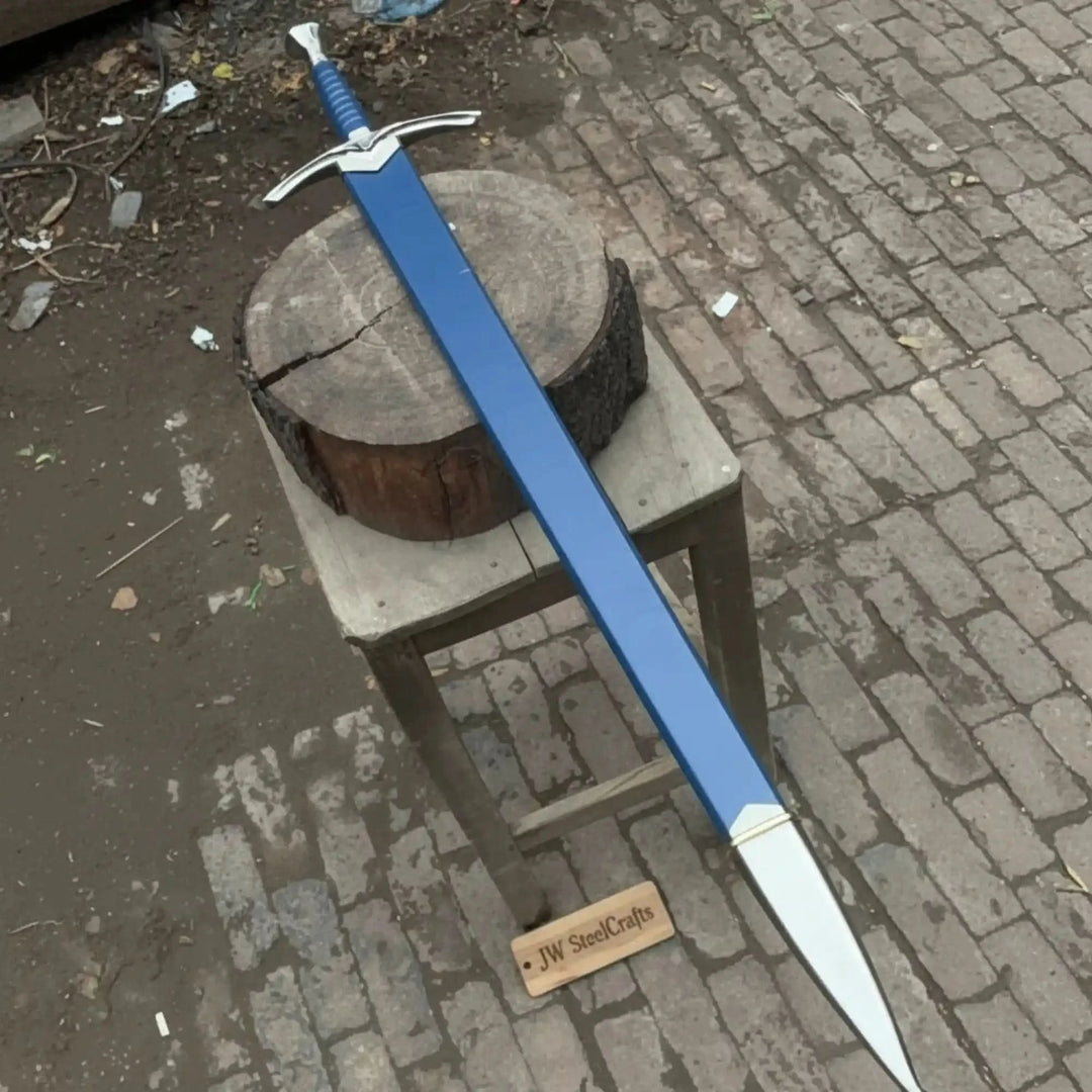 Full-length view of a medieval longsword and matching blue scabbard on a rustic wooden stool on cobblestones, highlighting the silver winged crossguard and blue wrapped handle.