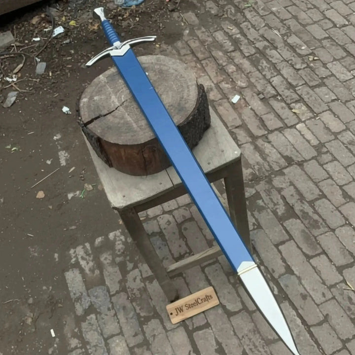 Full-length view of a medieval longsword and matching blue scabbard on a rustic wooden stool on cobblestones, highlighting the silver winged crossguard and blue wrapped handle.