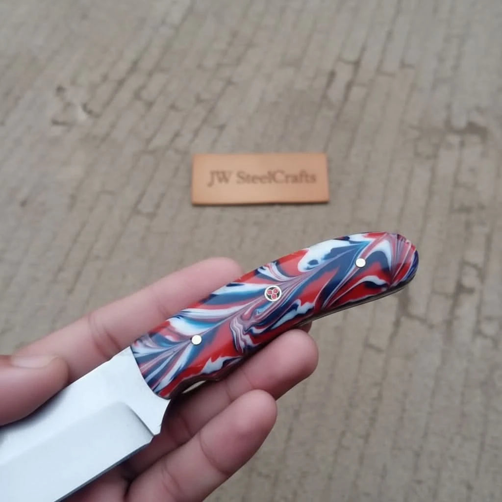 Polished skinner blade with red blue handle, brass rivets, and blurred forest campsite background.
