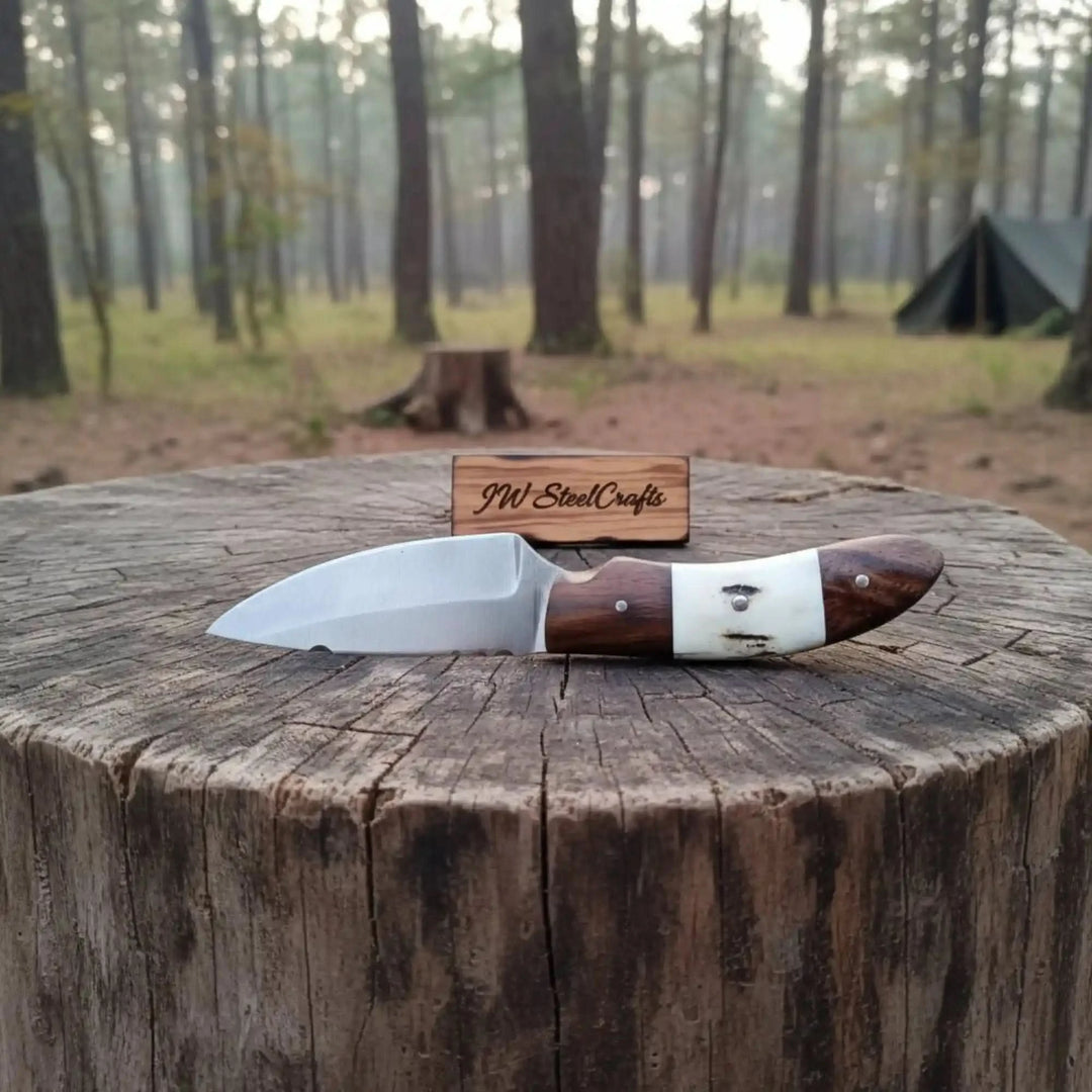 camping knife with polished blade, wood and bone handle, and JW SteelCrafts tag on a forest tree stump.