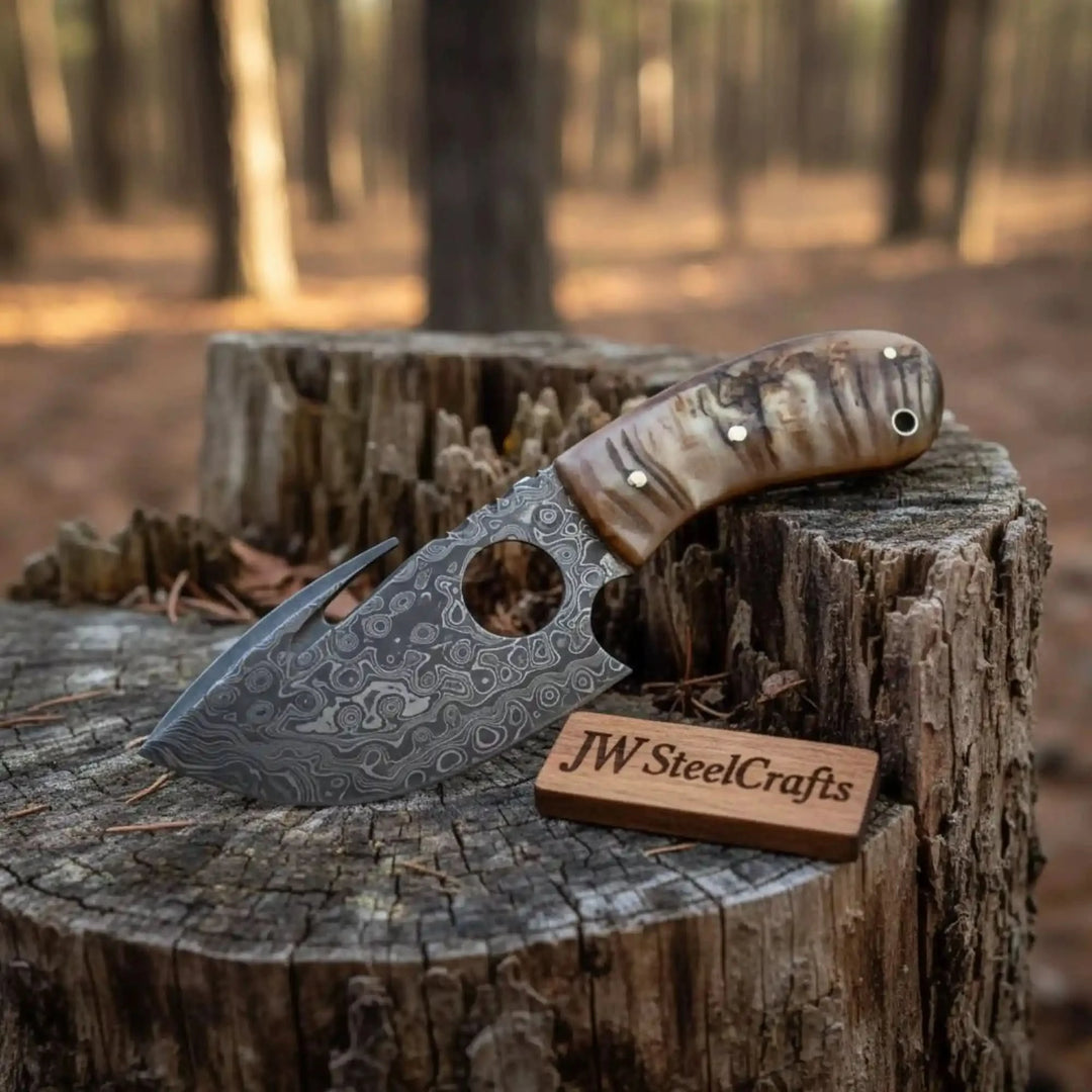 Decorative Damascus hook knife with stag handle, round finger hole, white rivets, and rustic stump surface.
