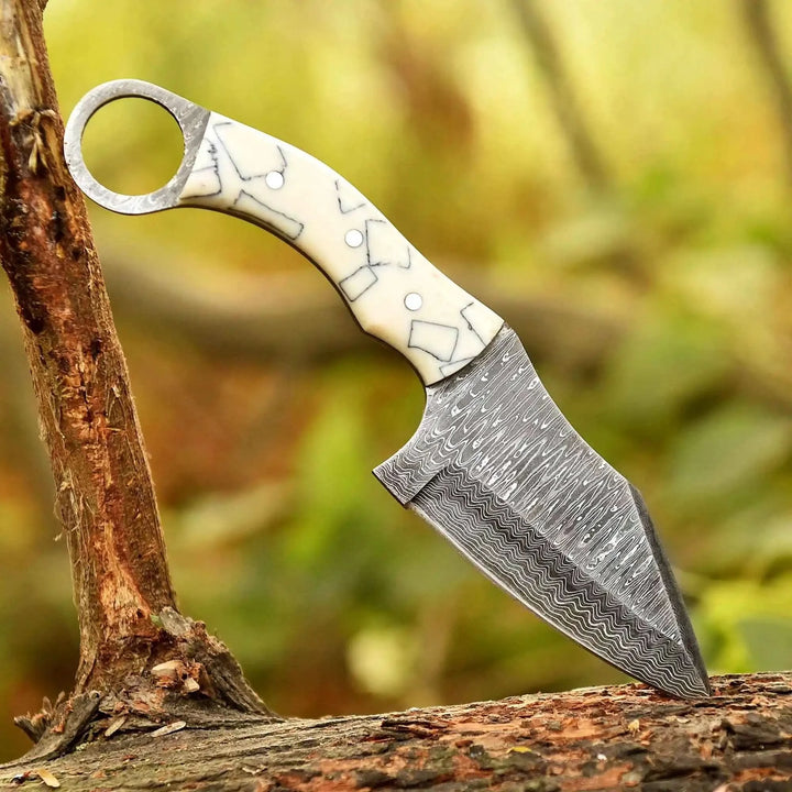 Patterned Damascus blade ivory handle knife resting on bark with a circular ring pommel and etched steel finish.