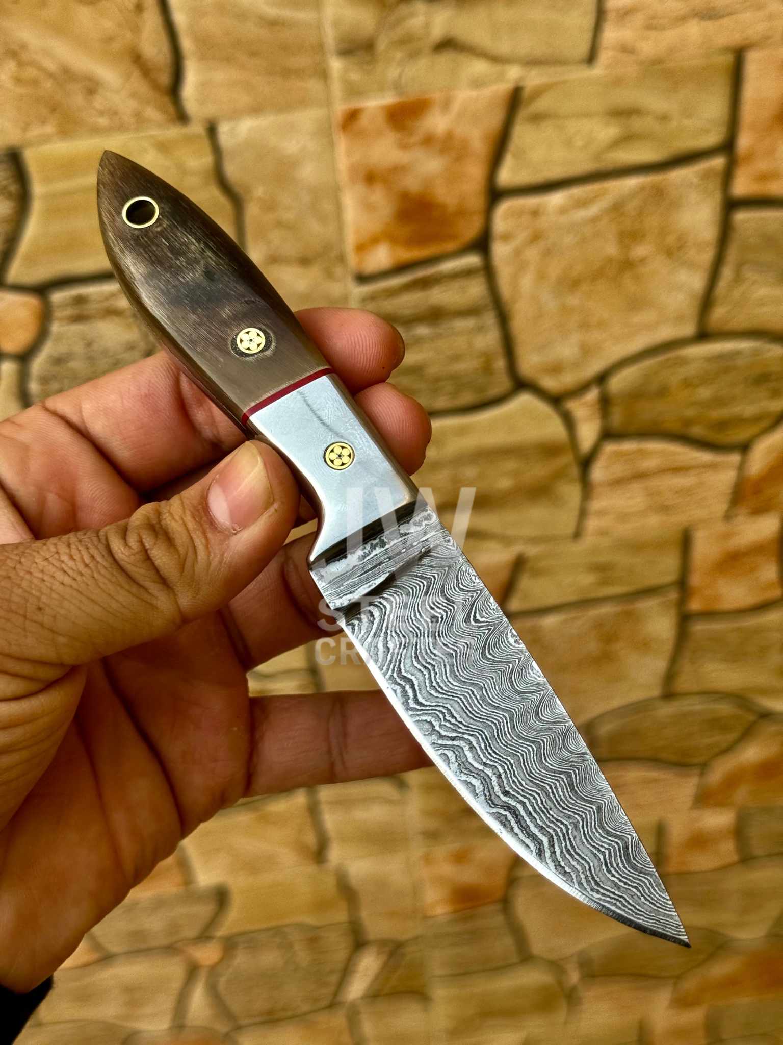 Hand holding a knife with a decorative blade against a stone wall background