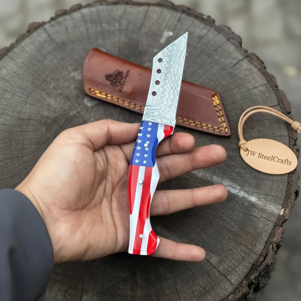 Handmade USA flag Damascus knife with stars and stripes handle, stitched brown leather sheath, and rustic stump background.