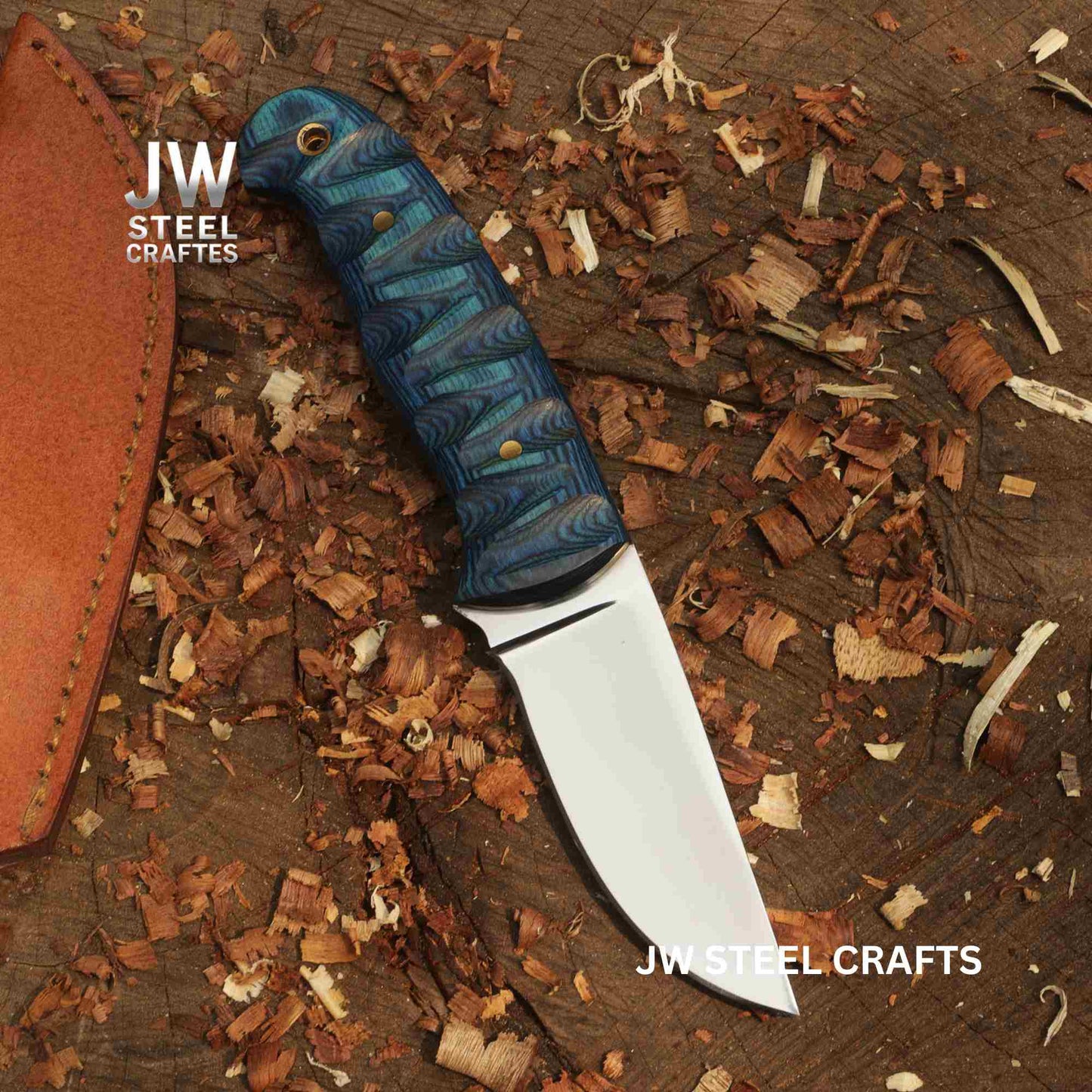 Knife with blue handle and leather sheath on a wooden surface with 'JW Steel Crafts' branding.