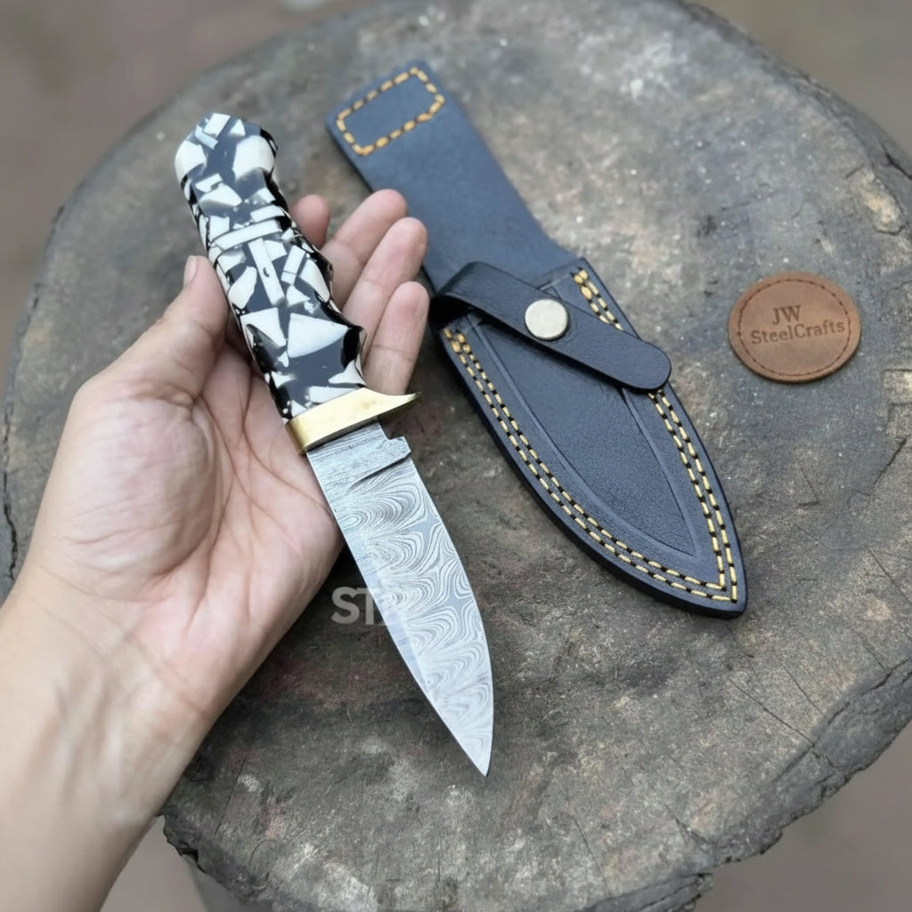 Monochrome handle custom small fixed blade knife with brass guard and patterned steel blade held in a hand.