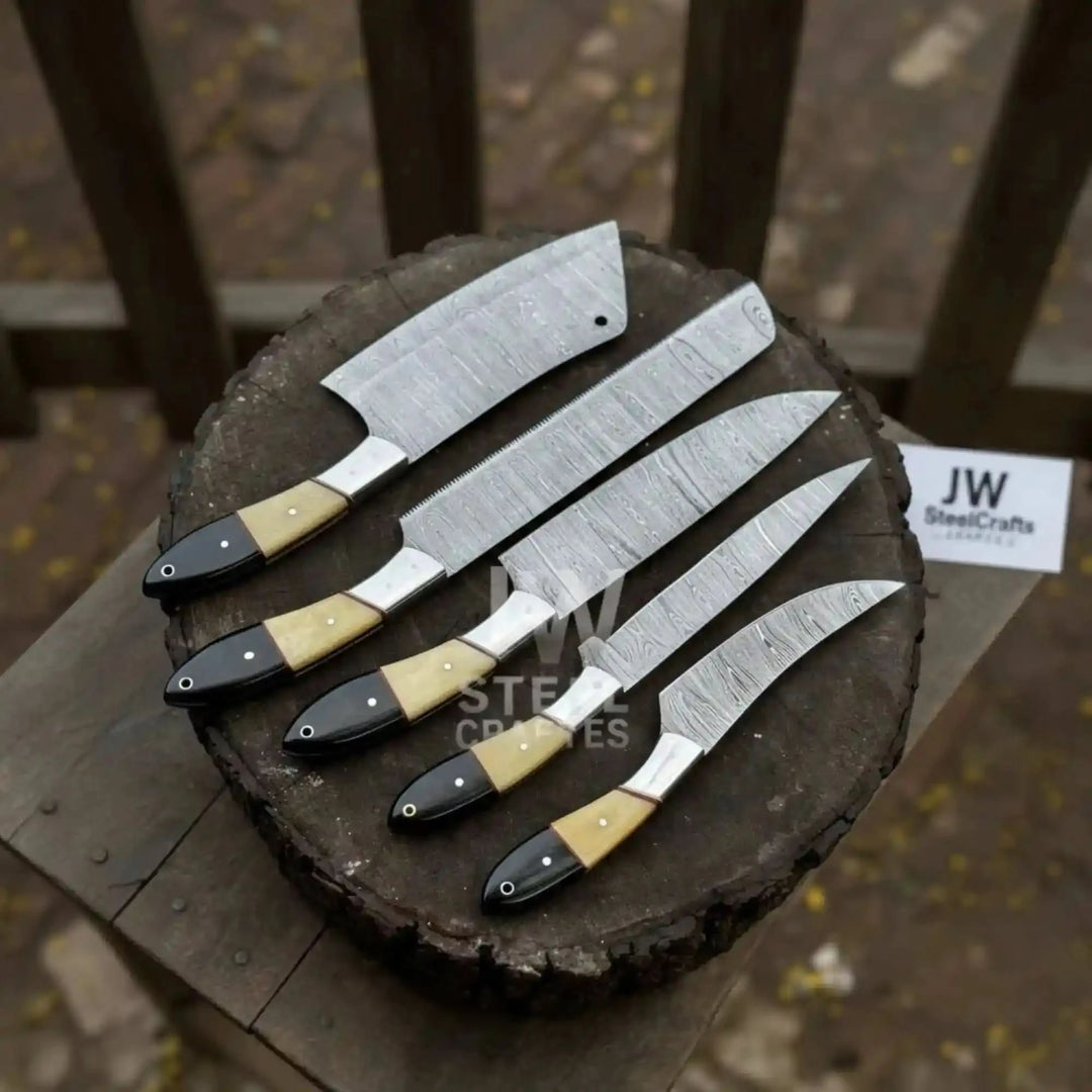 A 5-piece handmade Damascus steel chef knife set with elegant camel bone and black micarta handles, showcased on a rustic wooden log with a scenic blurred outdoor background.
