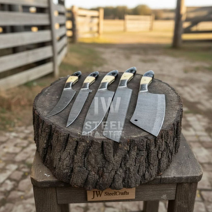Side view of a 5-piece handmade Damascus steel knife set with cream and black resin handles, arranged on a rustic tree log in an outdoor setting.