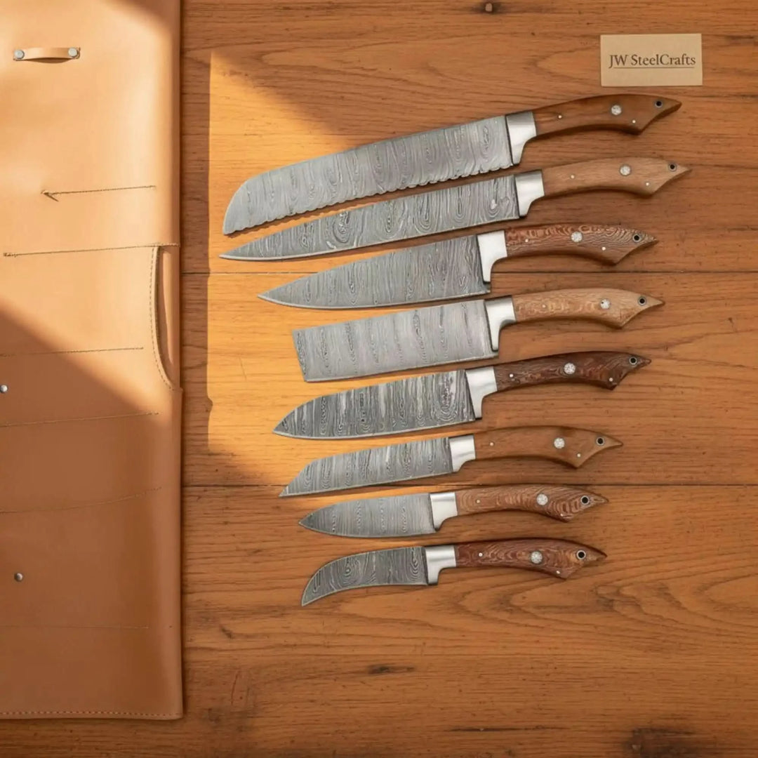 Wood handle Damascus knives arranged beside a leather knife storage roll on wooden boards.