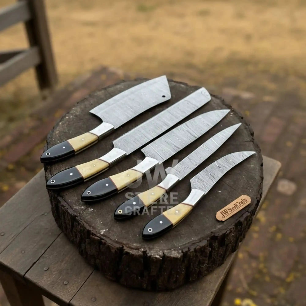 Handmade 5-piece Damascus steel chef knife set with cream and black resin handles, elegantly arranged on a natural tree log outdoors.