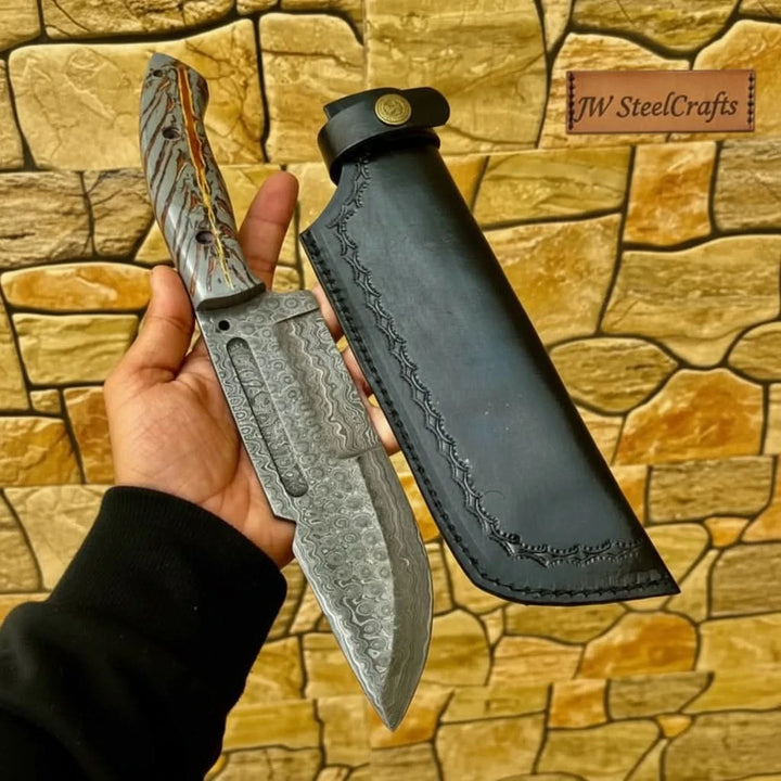 Handmade Damascus cleaver with thick patterned blade, decorative handle scales, and black stitched leather sheath.
