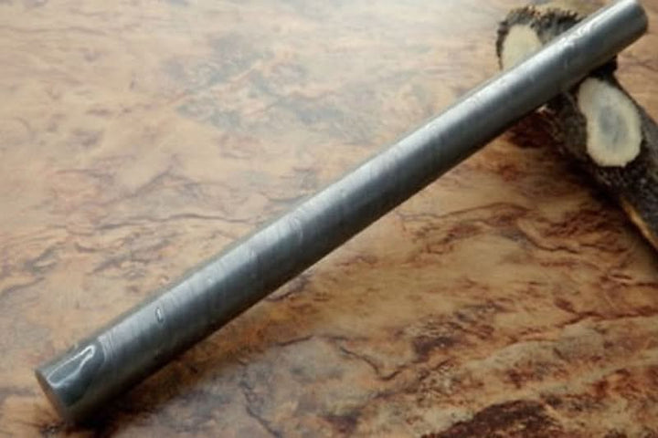Long round Damascus steel bar stock with subtle layered pattern placed on wooden surface for handmade knife making projects