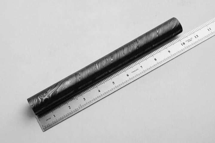 Damascus steel round bar with layered wave pattern placed beside measuring ruler for knife making and metal craft material sizing