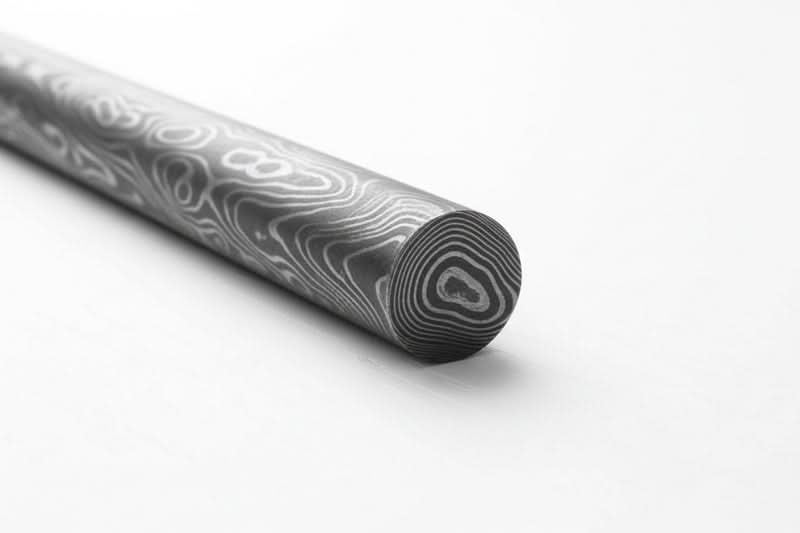Close-up of a Damascus steel round bar showing layered circular grain pattern and polished surface for knife making materials