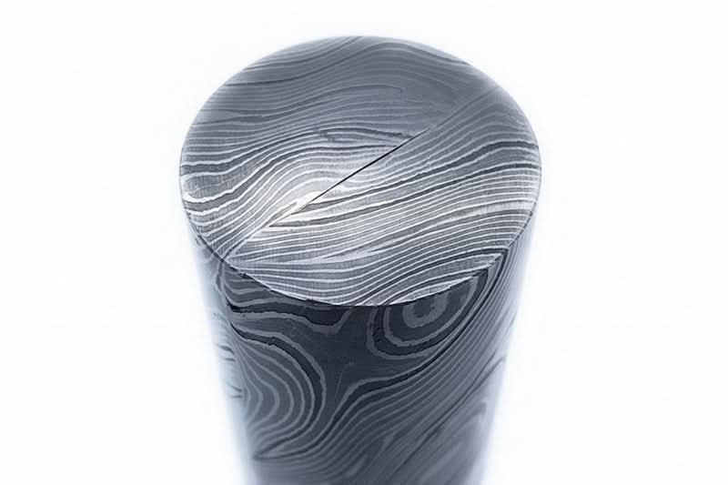 Close-up view of a round Damascus steel bar showing layered pattern details and polished surface for knife making materials