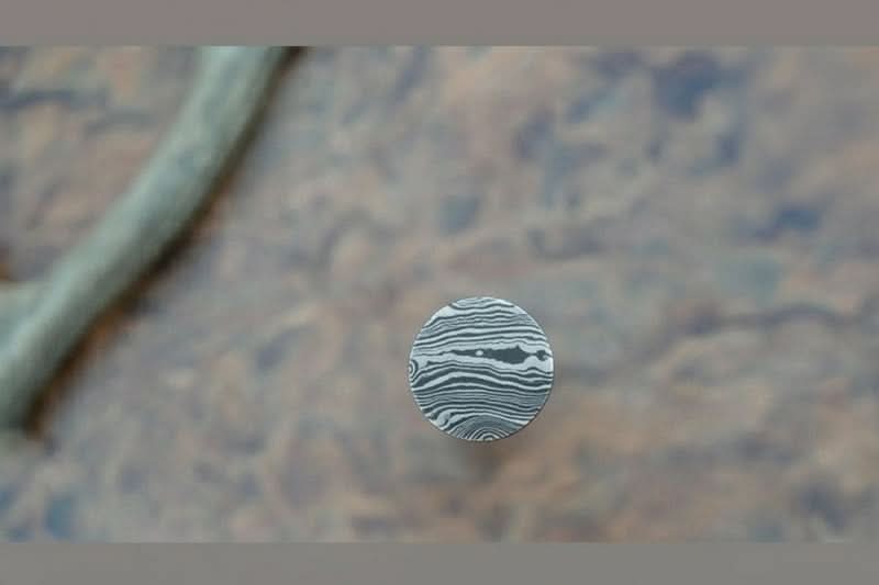 Close-up view of patterned Damascus steel round bar end showing layered wave grain detail for knife-making projects