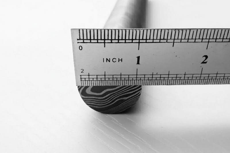 Damascus steel round bar end with layered grain pattern shown beside inch ruler for measuring knife making material dimensions