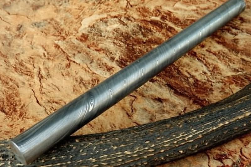 Round Damascus steel rod bar with visible layered grain pattern displayed on rustic wooden background for knife making materials