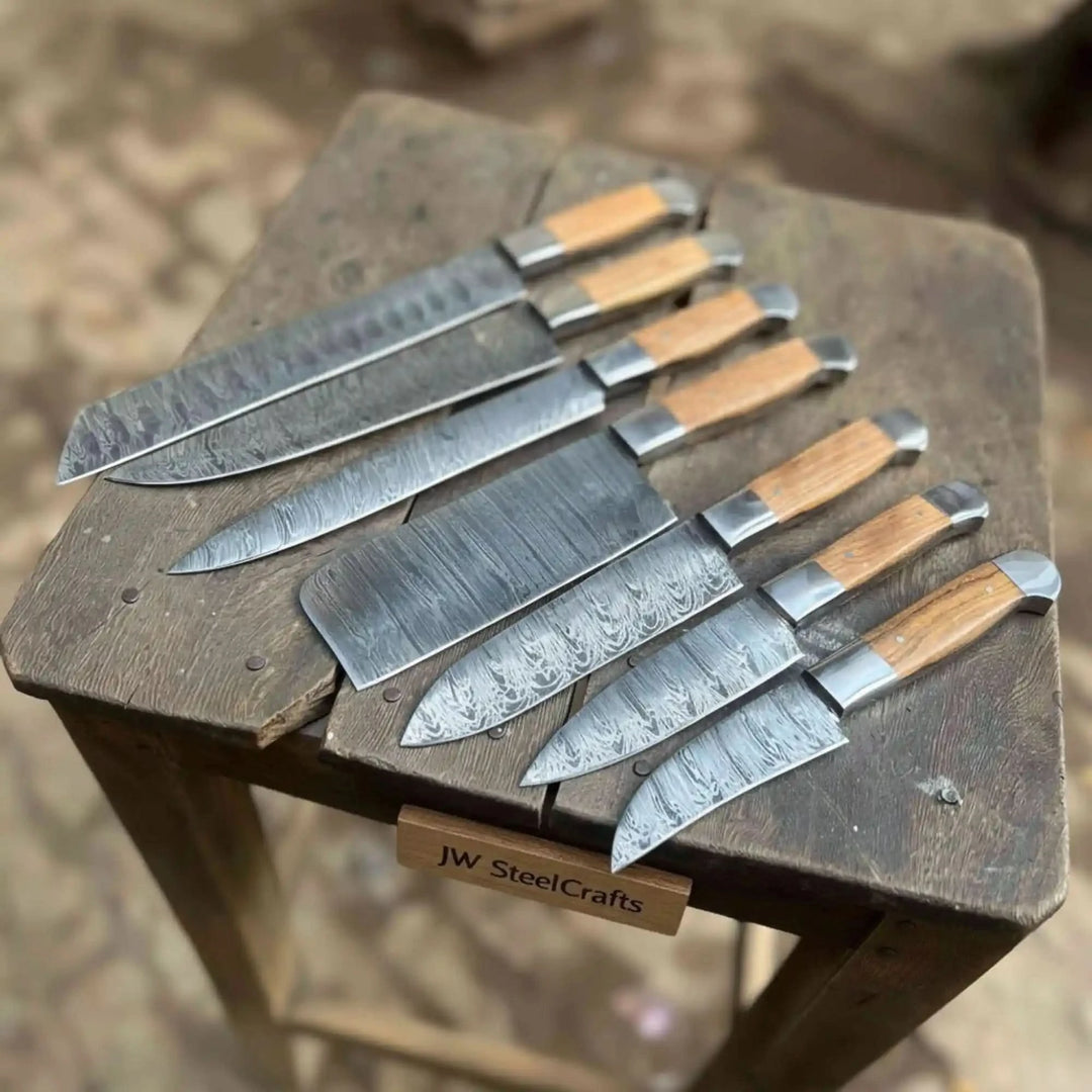 Eight-piece handmade Damascus steel kitchen knife set with olive wood handles displayed on a rustic wooden stool 
