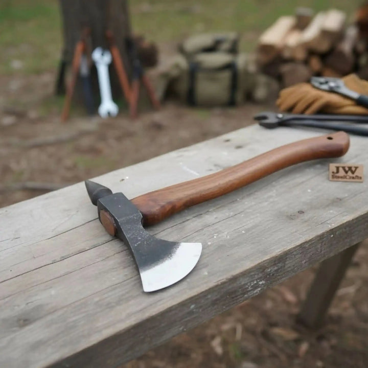     Forged bushcraft pick axe with polished steel blade and hardwood handle resting on a rustic outdoor wooden workbench.
