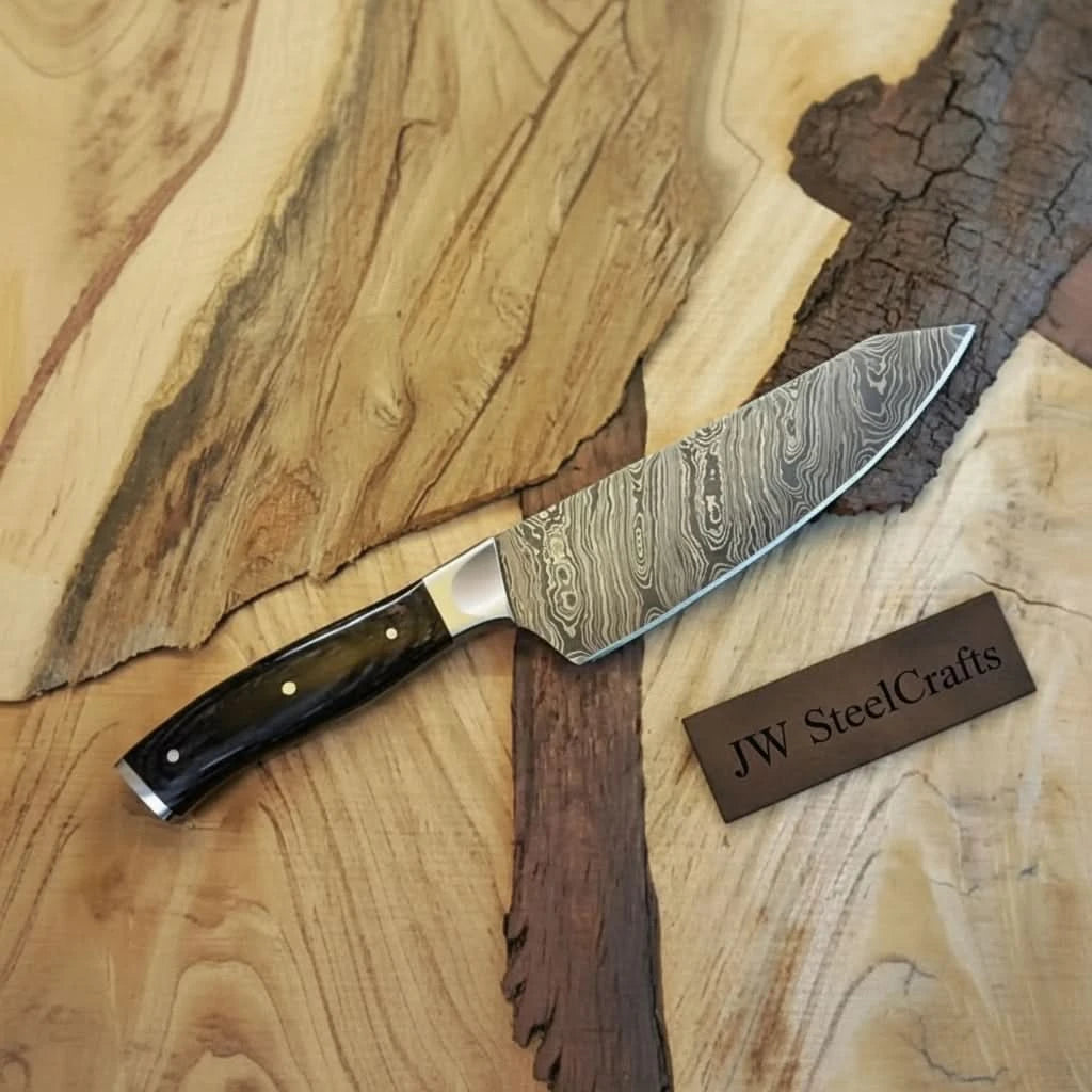 Broad Damascus blade with black handle and bright cutting edge on natural wood boards