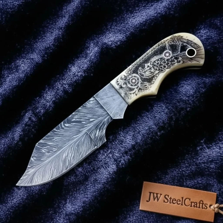 Carved bone handle Damascus fixed blade knife with detailed artwork, black lanyard hole, and swirling steel pattern blade.