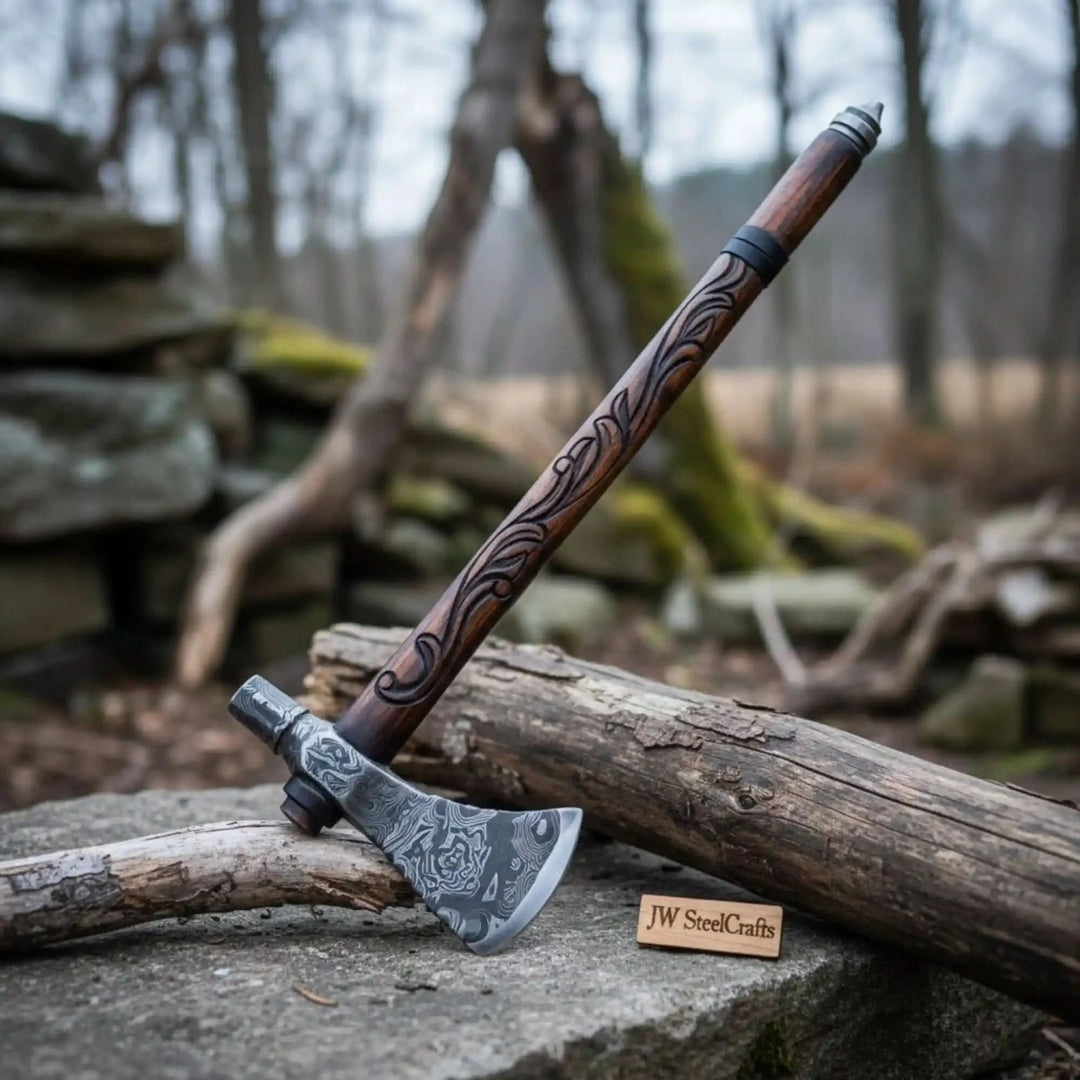     Handmade Damascus steel Viking hammer axe with carved wooden handle and black leather sheath resting on a forest stone backdrop.