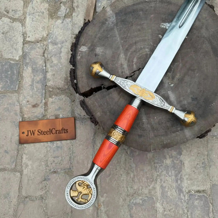 Collectible medieval-style sword with detailed gold engravings and red wooden grip displayed on a rustic tree stump