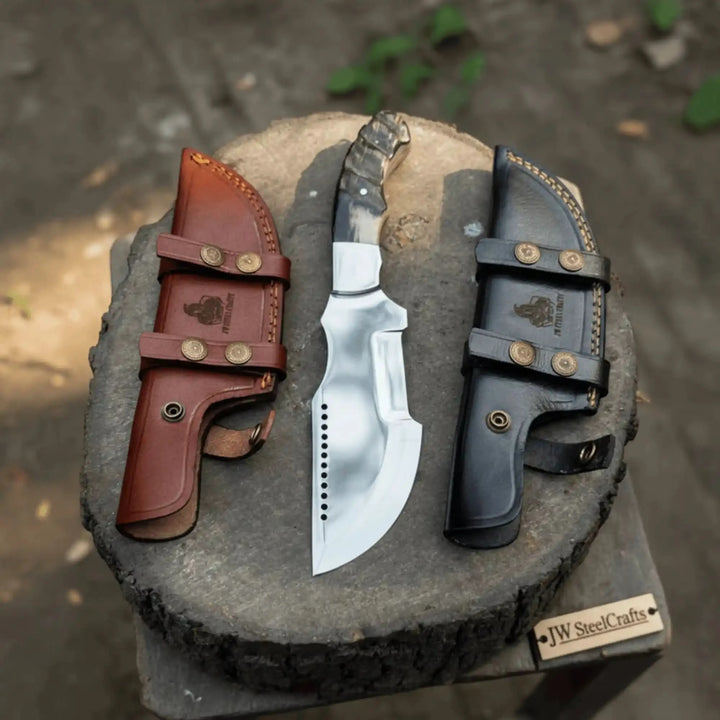 Handmade fixed blade knife displayed on a wood stump with one brown leather sheath, one black leather sheath