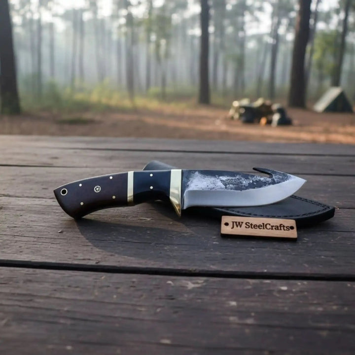 Outdoor hunting knife with gut hook blade placed on a wooden table against a blurred forest camping background.