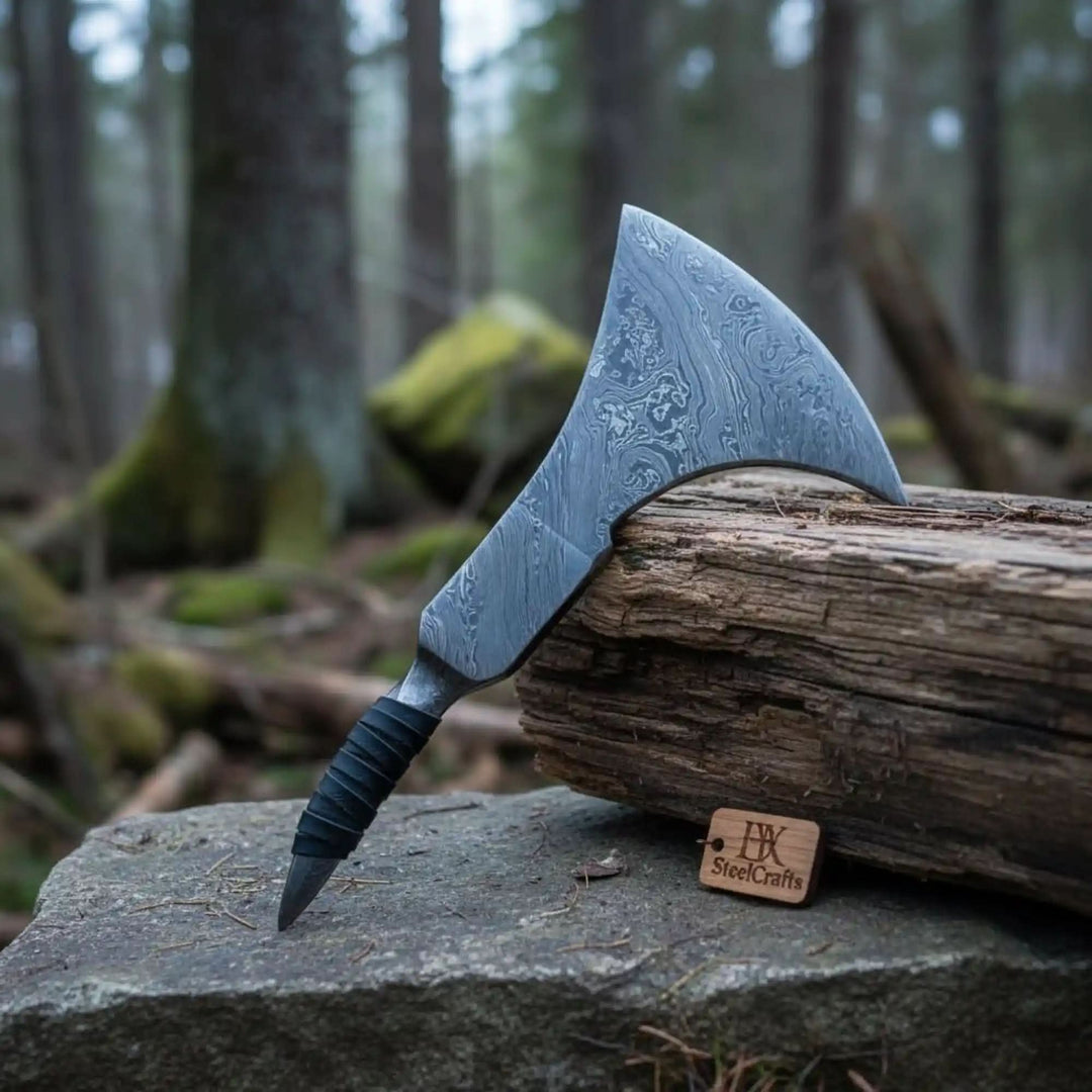     Heritage forged Damascus bushcraft axe with broad curved blade beside rugged timber log