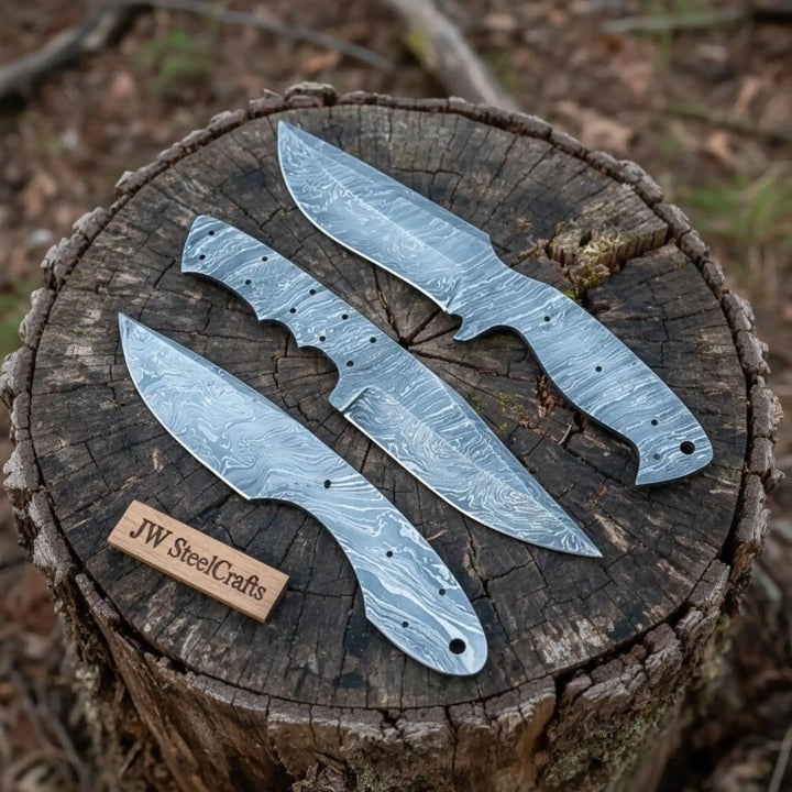 Unfinished full tang Damascus blade set with three patterned knives arranged on a rustic tree stump